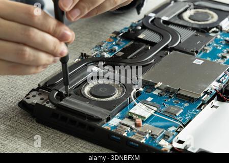 A person uses a screwdriver to open a laptop and access its internal parts in a clean tech workspace. The scene shows focus on repairing or upgrading Stock Photo