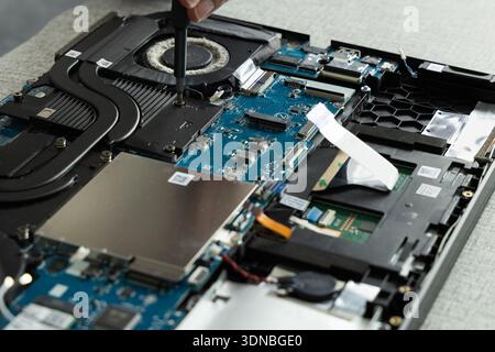 A person is repairing a laptop motherboard by using a tool to unscrew different parts. The work takes place at a repair shop in the afternoon. Stock Photo