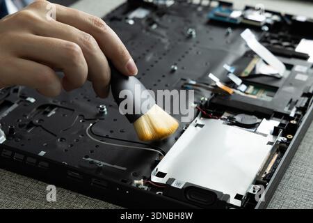 A person works on a laptop by carefully cleaning its interior with a brush. They focus on removing dust and dirt from the components. Stock Photo