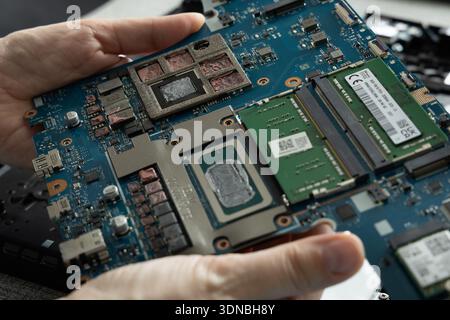 A person holds a circuit board in their hands, revealing various computer components. The setting is a workspace with tools around. Stock Photo