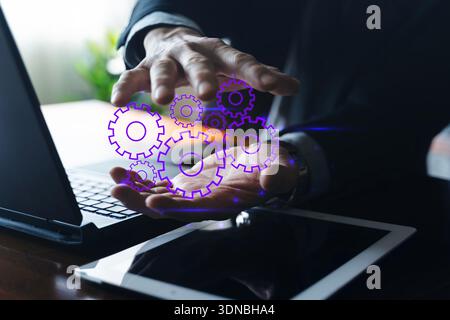 Hands of businessman controlling virtual gears above laptop, symbolizing digital transformation, software development, workflow optimization, and IT p Stock Photo