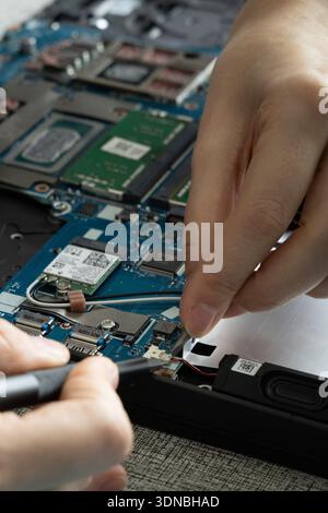 Hands work on a laptop's internal parts, connecting wires and examining circuit boards. Stock Photo