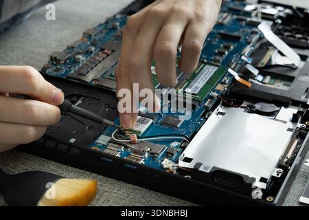 A person is focused on fixing a laptop in a home office. They are handling the internal parts and using tools for the repair. Stock Photo