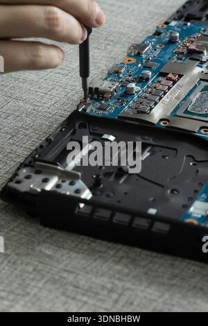 A person is repairing a laptop on a table. They hold a screwdriver and are fixing the internal components of the laptop. Stock Photo