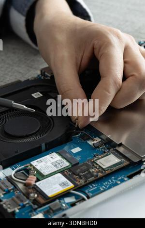 A technician works on a laptop motherboard in a workstation. The person uses tools to fix the internal components. Stock Photo