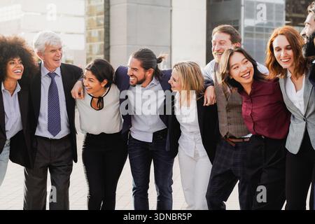 Group of multigenerational business celebrating and hug with office buildings on background - Businesspeople with diverse age and ethnicity concept Stock Photo