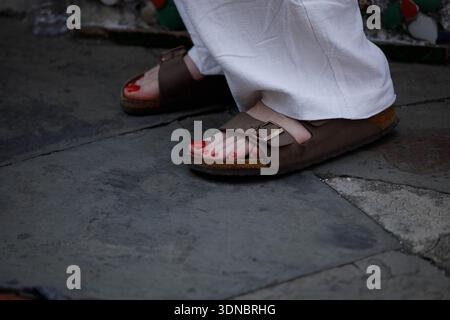 Woman in brown sandals standing on stone pavement, red toenails, foot and nail skin texture, high angle view Stock Photo