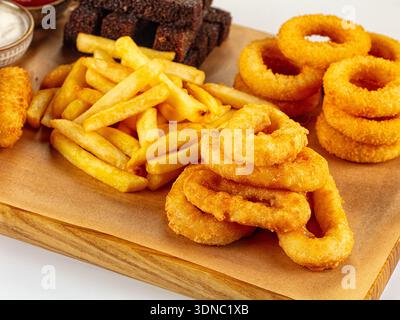 Assorted fried snacks on a wooden board, isolated on white. Golden onion rings, fries, cheese sticks, and rye croutons with ketchup and white sauce. P Stock Photo