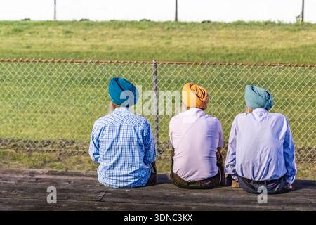 Senior bearded Sikh men enjoying spending quality time after retirement in village. Rear view of three old Sikh man with colorful turbans sitting outd Stock Photo