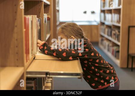the child chooses books on the shelf. A teenager chooses literature to read. Books on the shelves of a bookstore. Learning from books. The benefits of Stock Photo