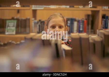 the child chooses books on the shelf. A teenager chooses literature to read. Books on the shelves of a bookstore. Learning from books. The benefits of Stock Photo