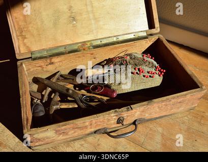 Old and worn wooden toolbox filled with vintage upholstery tools, including needle cushion, scissors, awl and hammers, all aged and rusty. The box sit Stock Photo