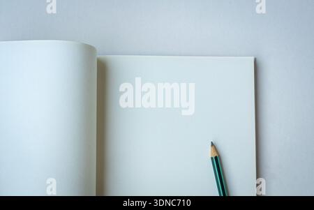 Pencil on top of an open blank notepad. Isolated on white surface. Space for text. Stock Photo