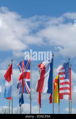 Colorful west flags representing various nations wave proudly on tall poles, showcasing a vibrant display against a bright blue sky with fluffy white Stock Photo