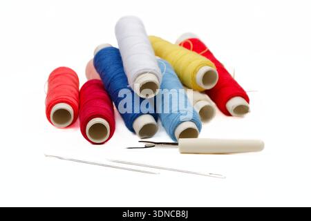 The photograph captures a bright, layered still‑life where red, blue, yellow, and white thread spools overlap partially, surrounded by sewing needles Stock Photo