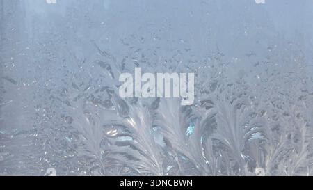 Beautiful ice crystals and frost patterns on window glass in winter. Natural cold-weather texture with soft blue tones. Ideal for seasonal backgrounds Stock Photo