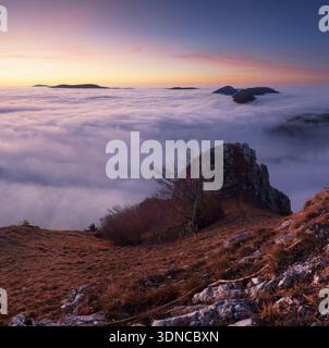 Sunset with clouds, sun rays, and misty valleys witn forest, mountain and peak nature landscape. Stock Photo