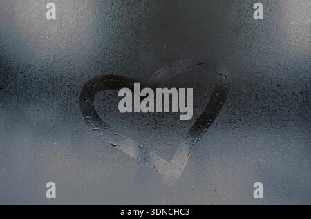 Heart Shape Drawn on Steamy Window Glass with Water Droplets Stock Photo