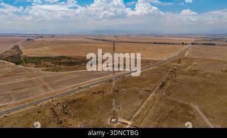 Aerial view of a tall red and white communication tower piercing the expansive landscape, contrasting with the dry fields and distant mountains, Cape Stock Photo