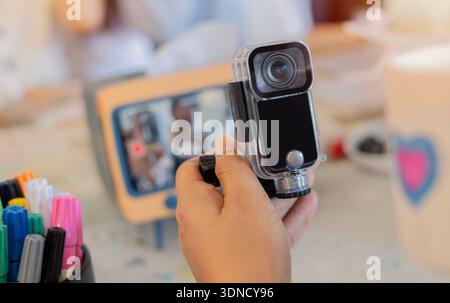 A small action camera on hands of a young woman while sitting on an art table. Selective focus. Action camera concept. Stock Photo