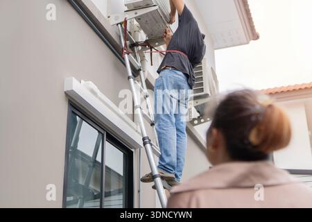 Mature Asian couple repairing their own air conditioner during their work break at home. Selective focus. Stock Photo