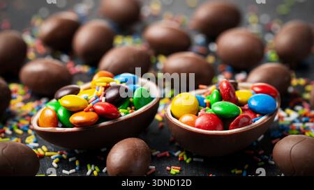Chocolate Easter eggs filled with colorful candy and sprinkles on dark festive background Stock Photo