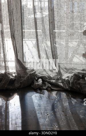 Soft morning sunlight shines through a translucent curtain with subtle textures, casting long shadows on a dark marble floor. Stock Photo