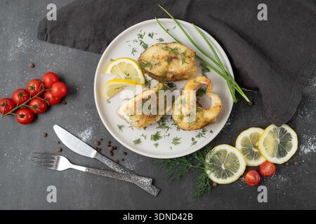 Baked zander fish with lemon, dill and cherry tomato on white ceramic plate with cutlery and linen serviette on brown stone board background. Stock Photo