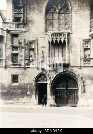 The richly carved Gothic façade of Maison Jacques Cœur rises above its arched entrances, with mullioned windows, sculpted figures and a projecting bay window dominating the stone frontage. Double wooden doors anchor the lower level, while a passer‑by provides scale. A 1927 architectural view of Bourges. From a collection of unique twentieth century photographs. Amateur photographer, snaps and some larger in a single album, charting one family's European travels. Stock Photo