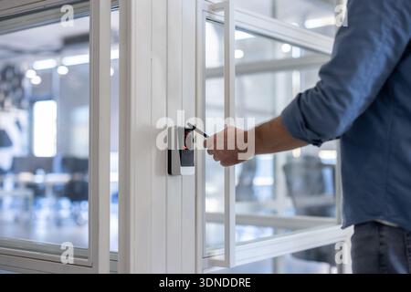 Person scanning key card on a sleek access control reader to unlock an office door, illustrating modern digital security, authorized entry, and everyd Stock Photo
