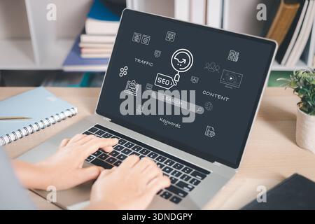 Hands typing on laptop displaying SEO and search marketing icons, analytics and keyword research concepts. Modern workspace scene for digital strategy Stock Photo