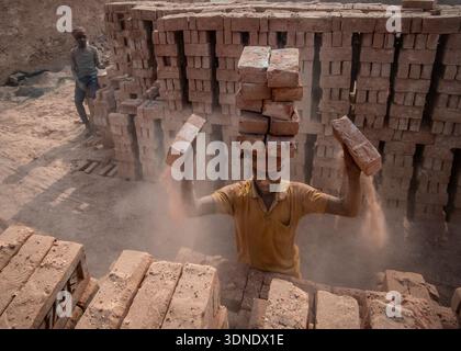 Dhaka, Bangladesh - 15 January 2019: View of a worker balancing bricks on his head amidst dusty brickyards, a testament to labor and resilience. Stock Photo