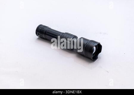 Black handheld flashlight lies on a light isolated background Stock Photo