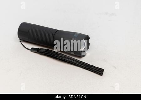 Black portable flashlight with strap lies on a light isolated background Stock Photo