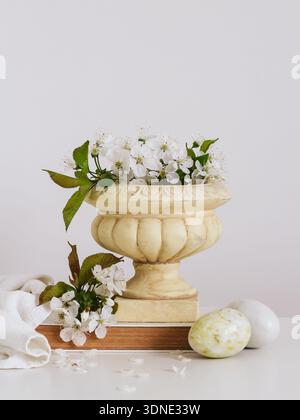 Spring composition with blooming cherry branches in a vase and decorative stone eggs on a bright background. Easter postcard with a copy space Stock Photo