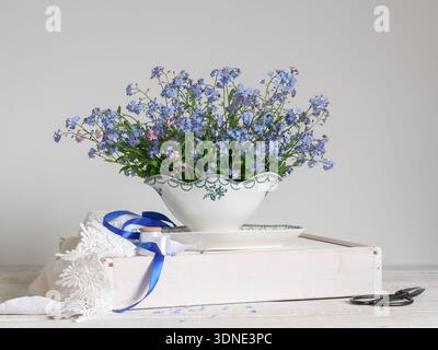 Bright still life with blue forget me nots in a vintage saucer on a white wooden table Stock Photo