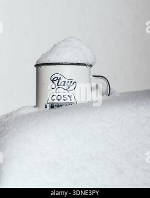 Close up of a white mug with the "Stay cosy" quote in a white snowy background Stock Photo