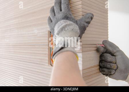 A person is installing ceramic tile panels in a home workshop while using tools and measuring carefully. Stock Photo