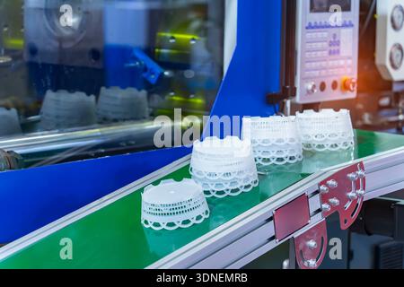Stack of polypropylene containers on conveyor belt of automatic plastic injection molding machine,automated technology concept Stock Photo