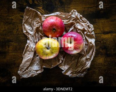 Three apples in a paper bag placed on a wooden table Stock Photo