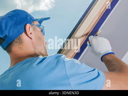 A man is working on painting a ceiling while standing on a ladder. Stock Photo