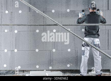 Worker uses tools to install insulation panels on a wall in a building under construction. Stock Photo