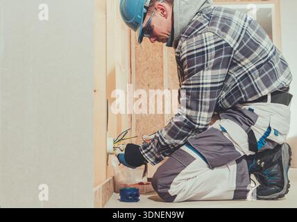 A worker connects wires to an electrical outlet in a new building during construction. Stock Photo