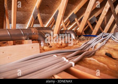 Workers are laying down ducts and insulation in the attic area. They focus on the airflow system. Stock Photo