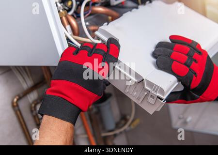 A person wears red and black gloves while fixing machinery. The setting shows pipes and tools. Stock Photo