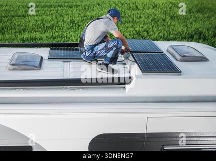 A person works on the roof of a camper by installing solar panels under clear skies. Stock Photo
