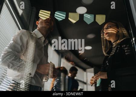 Two professionals discuss ideas in a glass-walled office with sticky notes and reflections Stock Photo
