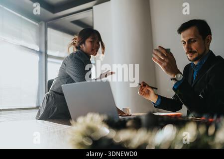 Two professionals collaborate in a bright office, discussing next steps over a laptop Stock Photo