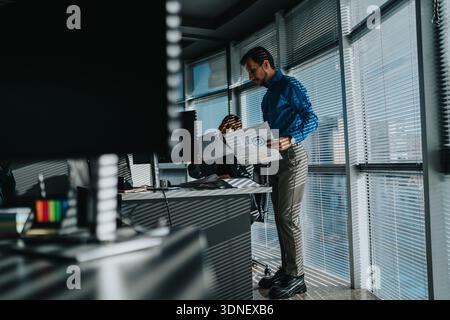 Professional man reviews charts in a bright office while a colleague works at a desk Stock Photo