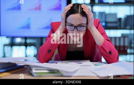 Stressful moments of a businesswoman analyzing charts in a modern office setting during a busy workday Stock Photo